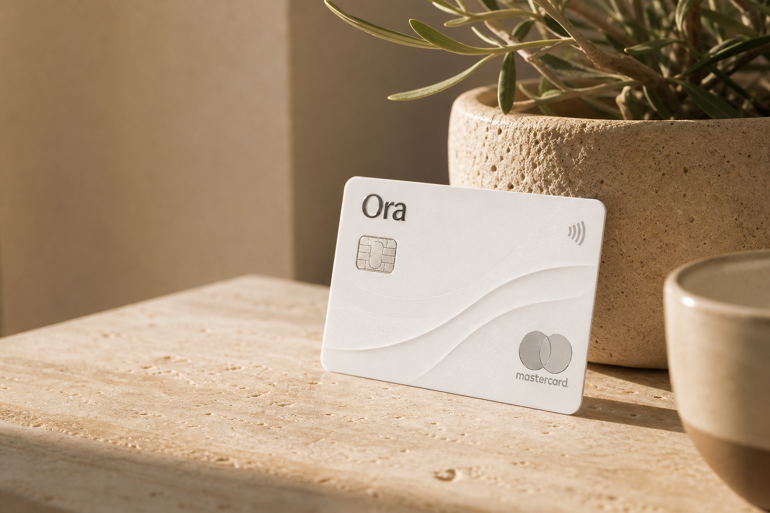 An Ora card resting on a sunlit travertine surface beside an olive plant
